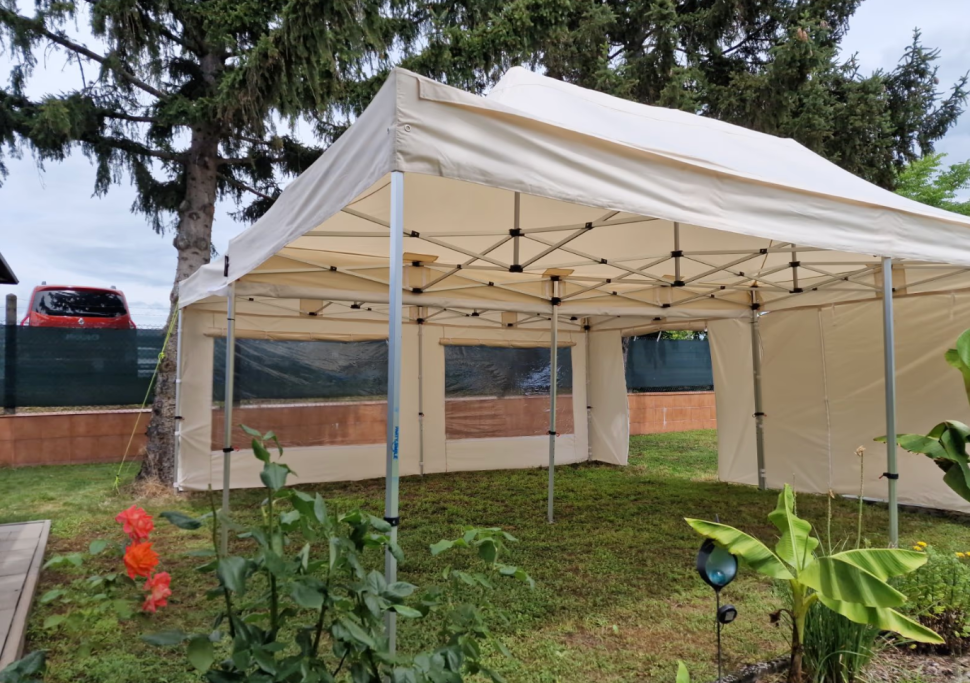 Faltpavillon Zelt in einem Garten mit geöffneten Seiten und grüner Vegetation im Vordergrund.