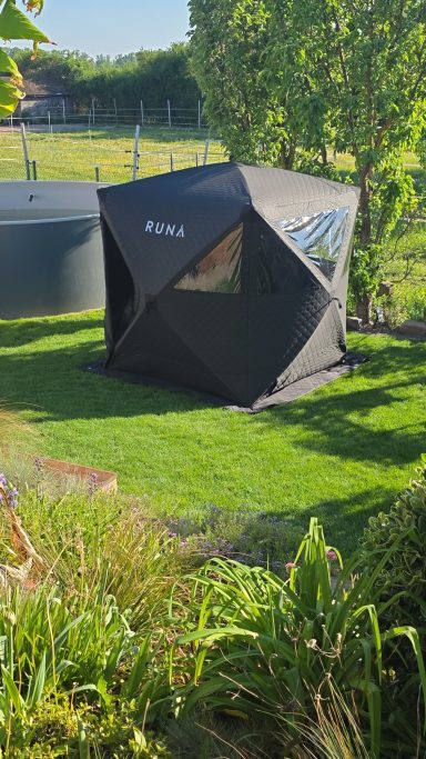 Zeltsauna Geometrisches, schwarzes Gartenhaus auf grünem Rasen, umgeben von Bäumen und Sträuchern.