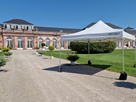 Zeltverleih Ein weißes Zeltdach steht vor einem historischen Gebäude, umgeben von Grünflächen.