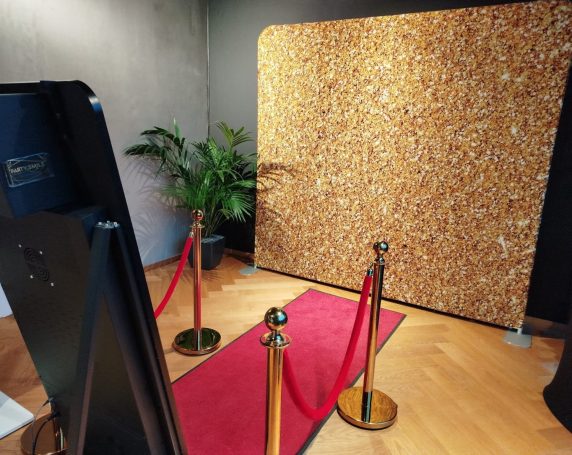 VIP-Absperrung Ein roter Teppich führt zu einer goldenen Wand mit roten Absperrseilen und einer Pflanze.