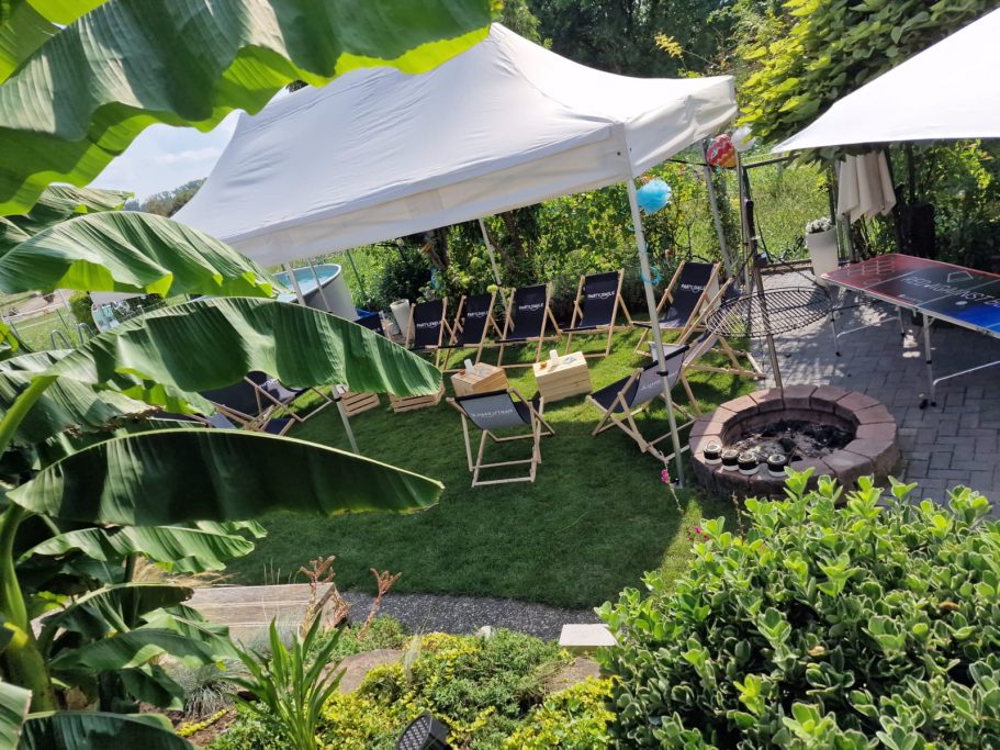 Flexibel & stabil Gartenmiete mit Zelten, Liegen und einem Feuerplatz umgeben von Pflanzen.