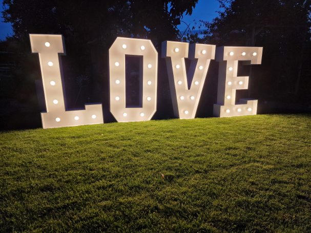 XXL Love Buchstaben Große, beleuchtete Buchstaben formen das Wort „LOVE“ auf einem grünen Rasen.