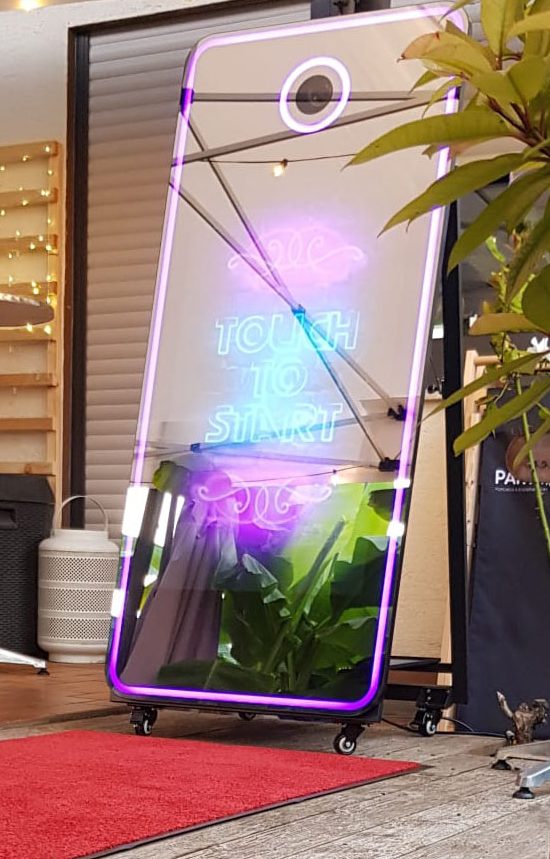 Magic Mirror Ein moderner Fotobox-Spiegel mit bunten Lichtern und Pflanzen im Hintergrund.