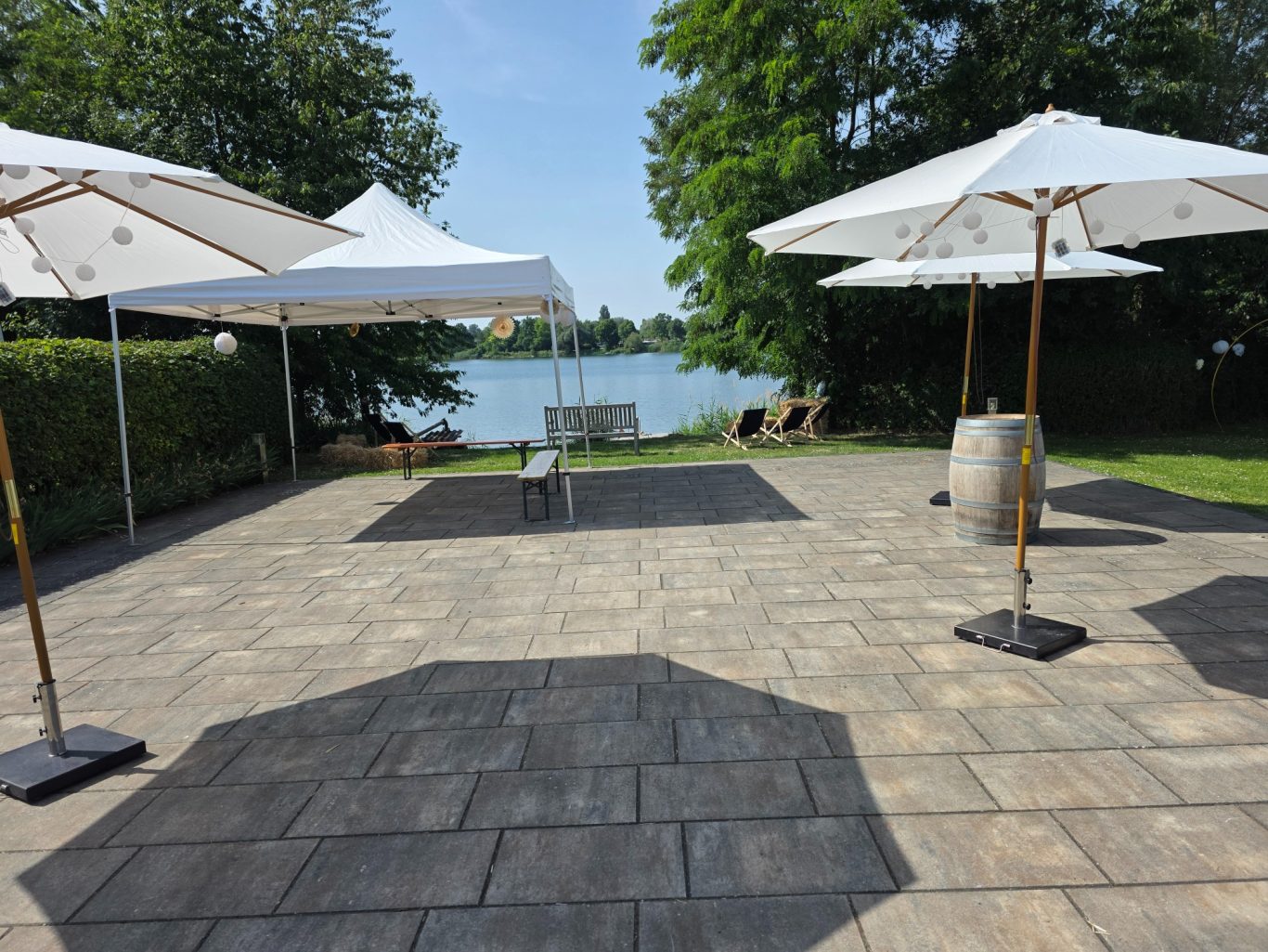 Sonnenschirme mieten Terrasse mit Sonnenschirmen, Blick auf einen See, umgeben von Bäumen und Gras.