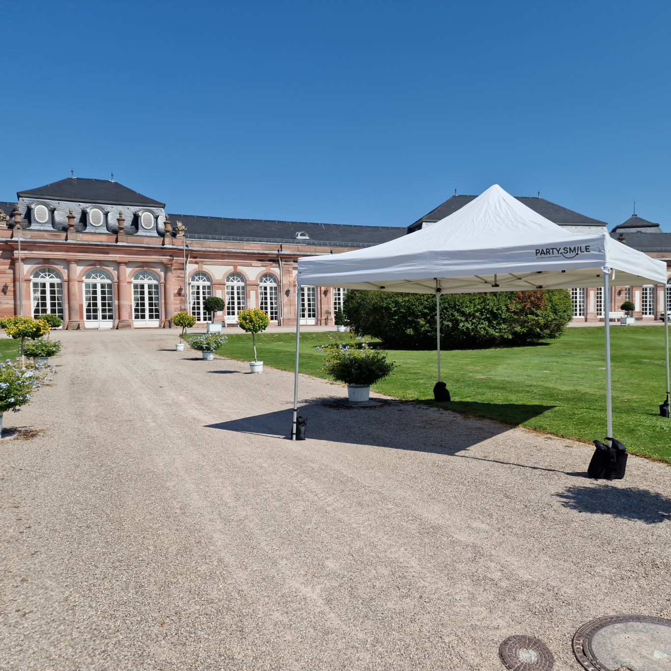 Faltpavillon Weißes Zelt auf einem gepflasterten Weg vor einem historischen Gebäude bei klarem Himmel.