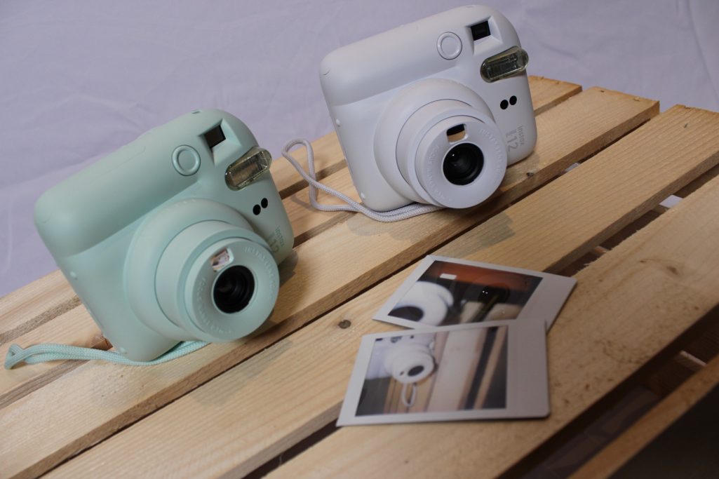 Sofortbildkameras Zwei Sofortbildkameras in Mintgrün und Weiß auf einem Holzbrett mit Fotos daneben.