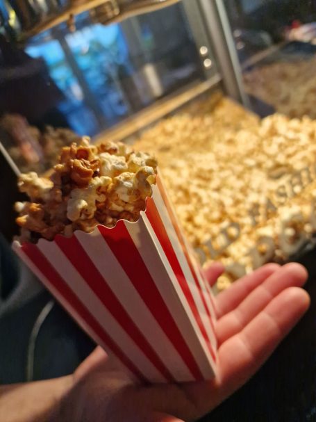 Popcorn Popcorn in einer roten und weißen Tüte, gehalten vor einem Popcornstand.